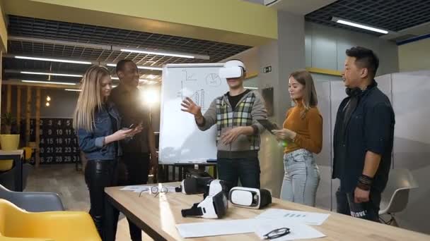 Caucásico centrado en el hombre en gafas de realidad virtual que se divierten jugando juego mientras sus vaqueros trabajan en la tableta, portátil . — Vídeos de Stock