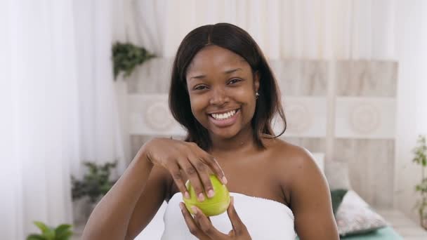 Smiling young African American woman holding apples slices in hands while posing smiling on the camera at wellness centre for body care — Stock Video