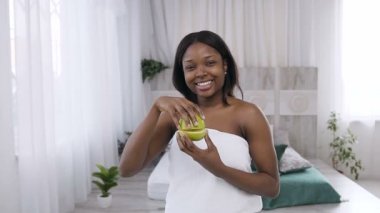 Spa'da kameraya gülümseyerek poz verirken elinde elma dilimleri tutan güzel genç Afro Amerikalı kadın. Sağlıklı yaşam tarzı, sağlıklı yaşam ve cilt bakımı konsepti