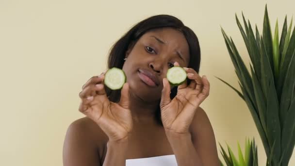 Tiro retrato divertido da bela mulher africana com pele lisa segurando uma fatia de pepinos, rejuvenescimento do regime de tratamento da pele conceito de beleza facial — Vídeo de Stock