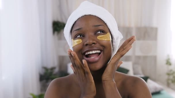 Porträt einer hübschen jungen Afrikanerin mit medizinisch goldenen Flecken unter den Augen, während sie im Schlafzimmer nach der Dusche steht. gesunder Lebensstil, Jugend, Gesichtsbehandlung, Anti-Aging — Stockvideo