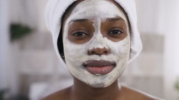 Attractive afro-american girl with white towel on head having a cleansing mask on face looking at camera — Stock Video