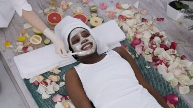 Güzel genç afrikalı kadın spa resort dinlenirken kozmetolojist yüzüne yüz maskesi uygular. Sağlık, gençleştirme yüz, cilt bakımı