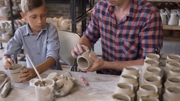 Petit garçon mignon avec son père faisant des pots en céramique dans la poterie . — Video