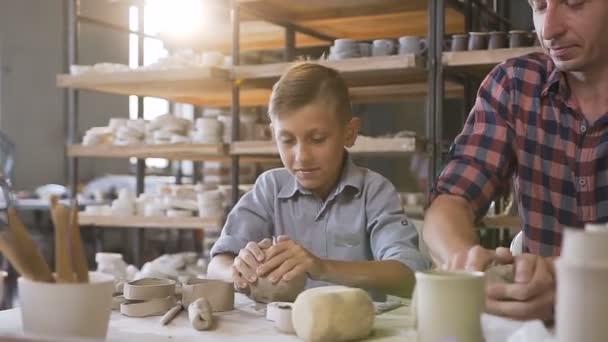 Père attentionné enseignant petit fils comment travailler avec de l'argile sur la roue des potiers . — Video