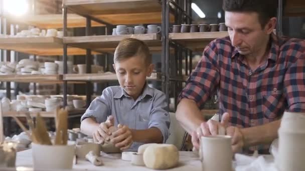 Attractive caucasian man and liitle cute boy kneading clay for pots. — Stock Video