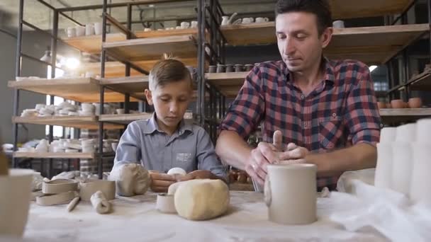 Petit garçon faisant partie de pots tandis que son père pétrissant de l'argile . — Video