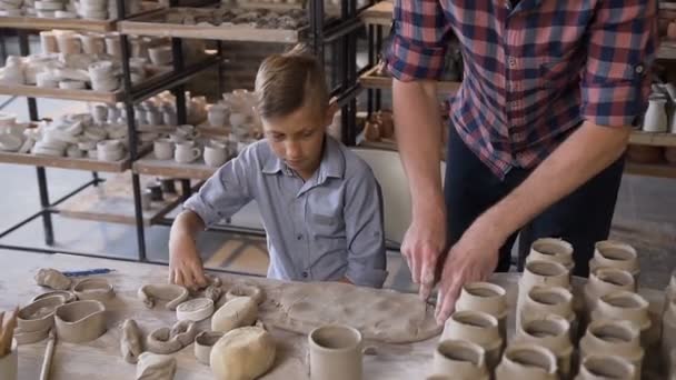 Kaukasischer Vater bringt kleinem Sohn bei, wie man mit Ton auf Töpferscheibe arbeitet. — Stockvideo