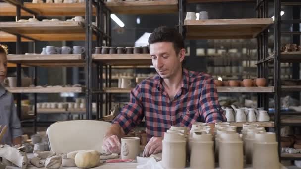 Gerichte mannelijke Potter maken keramische vaas terwijl kleine jongen naar hem komen. — Stockvideo