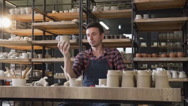 Oleiro masculino olhando para o boné artesanal durante o dia de trabalho na cerâmica . — Vídeo de Stock