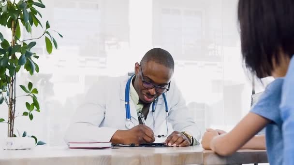Africano jovem médico dando receita para a mãe bonito com aqui filho na clínica . — Vídeo de Stock