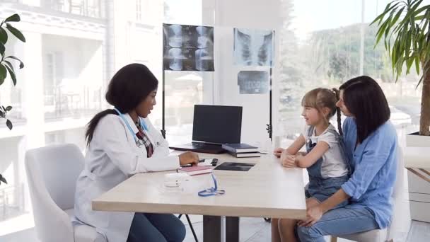 Lycklig kaukasiska mor med dotter pratar med afrikansk, amerikansk läkare på kliniken. — Stockvideo