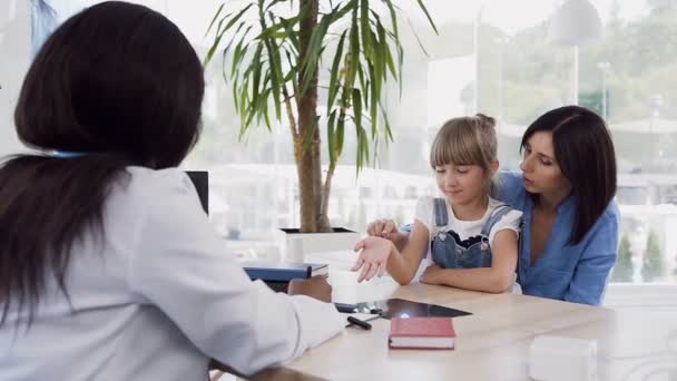 Niña sentada con rodillas de madre joven hablando con médico africano en el hospital . — Vídeos de Stock