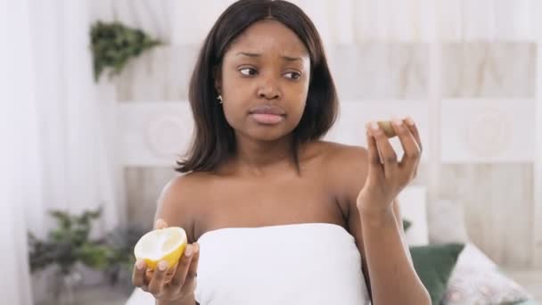 Naranja o kiwi. Divertido retrato de la hermosa mujer africana con la piel lisa sosteniendo una rebanada de naranja y kiwi, rejuvenecedor tratamiento tratamiento de la piel concepto de belleza facial — Vídeo de stock