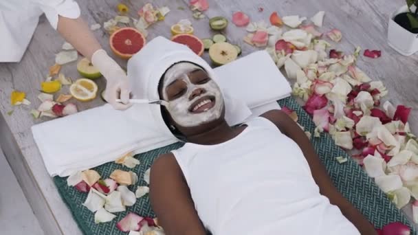 漂亮的年轻非洲妇女放松的顶视图，而美容师使清洁和滋润皮肤在水疗沙龙的程序 — 图库视频影像