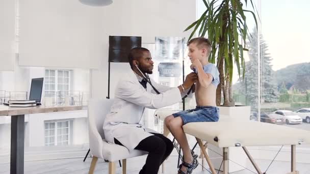 Африканский педиатр осматривает симпатичного мальчика, используя стетоскоп . — стоковое видео