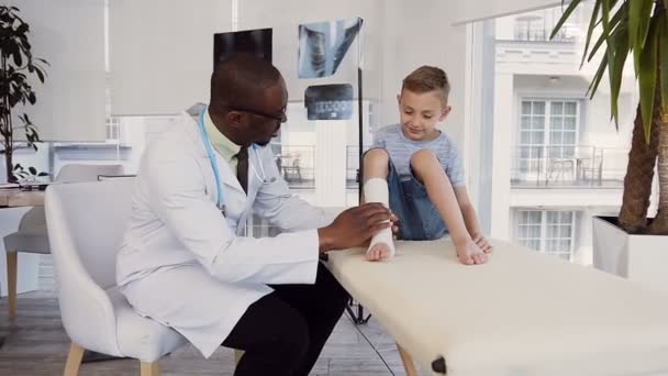 Male doctor bandaging leg of cute boy. — Stock Video