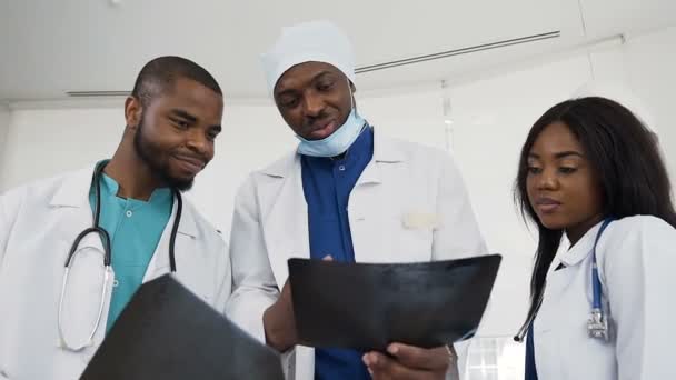 Drie arts bespreken geschiedenis van de ziekte met behulp van x-ray van pattient in het ziekenhuis. Ziekenhuis, beroep, mens en geneeskunde concept. — Stockvideo