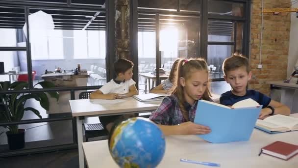 Grupp kaukasiska elever i grundskolan lärande självständigt i klassen medan manliga Koreanska lärare somesing förklarar och hjälpa två elever — Stockvideo