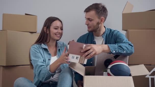 Excited young couple unpacking things, opening box and talking during moving to new apartment. — Stock Video