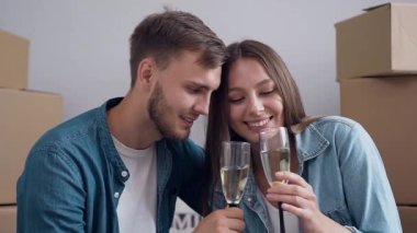 Genç adam ve kadın aşık klinking ve yeni daire, ev arka plan üzerinde şampanya içme.