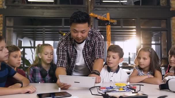 Team av sex unga kaukasiska nyfikna tekniker som arbetar tillsammans med sin lärare med hjälp av datorplatta i ingenjörs klass — Stockvideo