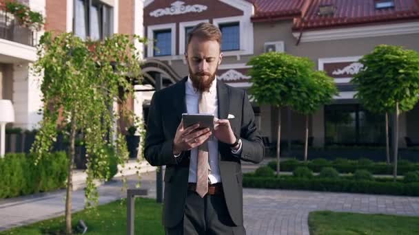 Eleganter schlanker Büroangestellter, der in der Nähe schöner Gebäude steht und sein Gerät für die Suche nach notwendigen Informationen für die Arbeit benutzt — Stockvideo