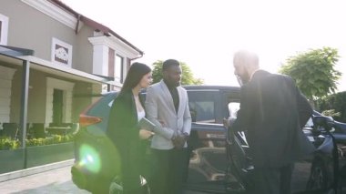 Zarif sakallı adam rahat evler arasında bahçesinde Afrikalı Amerikalı adam ve Avrupalı kadın için siyah bir araba gösteren