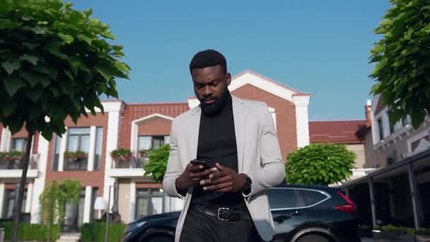 Серйозний молодий афроамериканець бізнесмен в чорно-білому костюмі ходіння по міській вулиці і розмовляти по телефону з діловим партнером — стокове відео