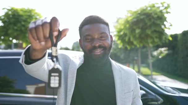 Sorrindo barbudo afro-americano mostrando carros chave em sua mão no fundo de seu carro comprado — Vídeo de Stock