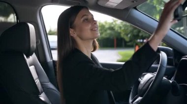 Sürücü koltuğunda oturan, aynaya bakan ve mutlu bir şekilde gülümseyen genç iş kadınının portresi