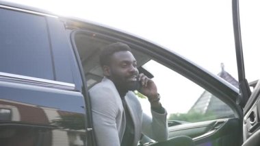 Beyaz ceketli gülümseyen sakallı Afro-Amerikan adam ön yolcu koltuğunda oturur ve telefonda konuşurken