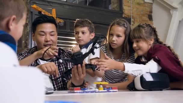 En la lección de física joven profesor asiático masculino demostrando helicóptero para los alumnos de la escuela caucásica en clase. Concepto de ciencia, drones, ingeniería y personas — Vídeo de stock