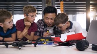 Elektronik mühendisi öğretmeni ve beyaz öğrenciler araba robotu modeli ile çalışıyor