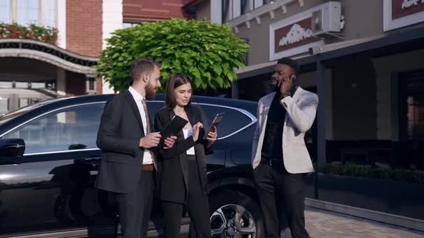 Çekici genç karışık ırklar iş adamları siyah araba yakınında duran ve işlerini tartışmak — Stok video