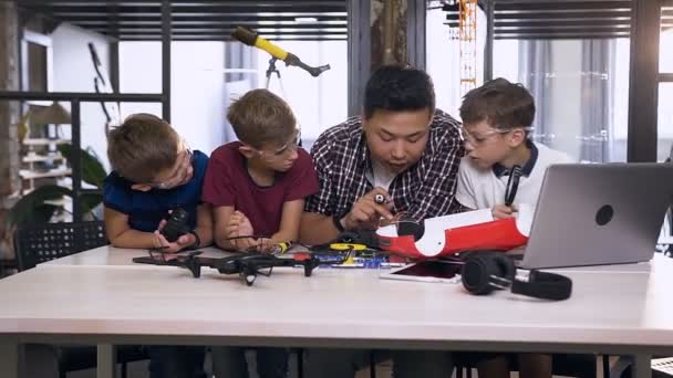 Команда молодых инженеров-электроников с корейским преподавателем использует отвертку во время работы паяльных проводов в образце автомобиля робота в современной школе — стоковое видео