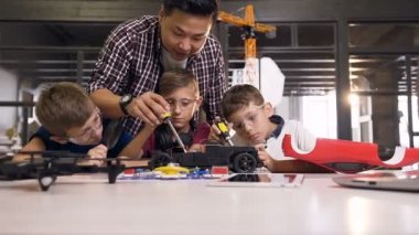 Asyalı erkek öğretmen yardımcı oluyor ve nasıl robot araba inşaat detay tornavida sabitleme kullanarak genç okul çocukları anlatıyor