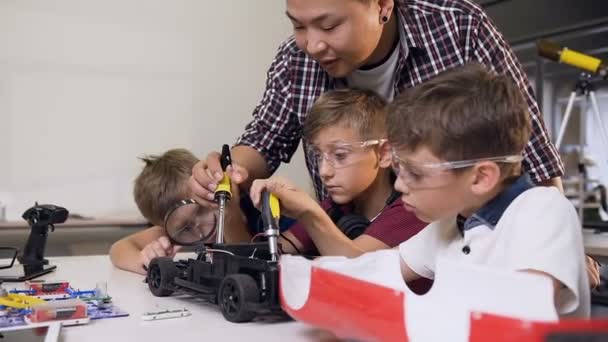 Mechaniker hilft Jungen mit Schraubendreher, Robotermaschinen auf dem Tisch im modernen, komfortablen Spielraum zu montieren — Stockvideo