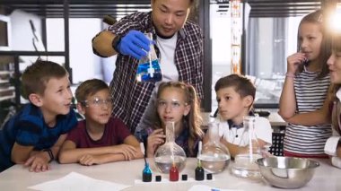 Erkek Koreli öğretmen sınıfta genç öğrencilere kimyasal deney gösterir. Cam şişesinde kimyasal reaksiyon mavi renk. Bilim, kimya ve bilim adamları