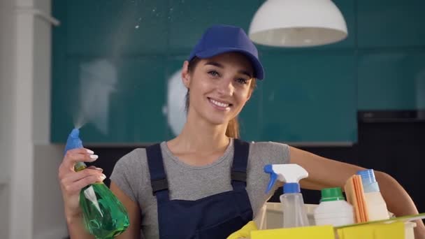 Menina dos anos 30 bonita em roupas de limpeza pulverizando o detergente verde no fundo da cozinha azul-preta — Vídeo de Stock