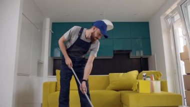 Yakışıklı sakallı adam paspas ve dans kullanarak mutfağında zemin temizlik iş elbisesi giymiş