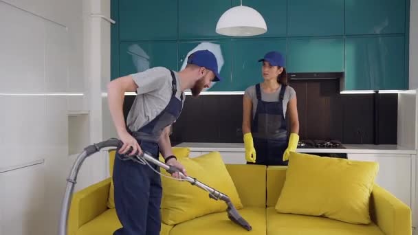 Limpieza de la trabajadora explicando las cosas masculinas cómo aspirar correctamente el sofá — Vídeos de Stock