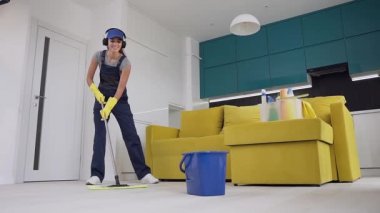 Kauçuk eldiven komik güzel temizlik işçisi onun kulaklık müzik dinleme ve zemin wipping sırasında bir mikrofon olarak bir paspas kullanarak