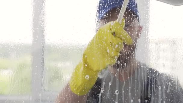 Limpador barbudo macho divertido em azul uniforme lavar a janela com spray de limpeza e espremedor especial — Vídeo de Stock