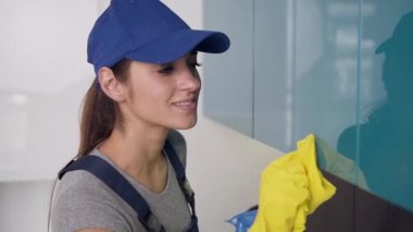 Üniforma ve sarı eldiven giymiş temizlik hizmeti güzel genç kadın işçi mutfak mobilyaları wipping