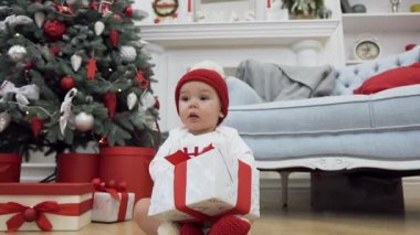 Noel dekore odanın arka planda güzel bir hediye ile katta oturan noel giysileri giymiş Tatlı bebek