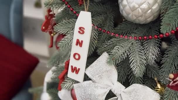 Árbol de Navidad festivo decorado con nieve, cinta plateada brillante, conos de pino y guirnalda roja — Vídeos de Stock