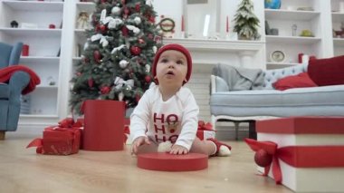 Güzel küçük bebek noel kutusunun kırmızı kapak ile oynarken şenlikli dekore yeni yıl odasıortasında ahşap zemin üzerinde oturan