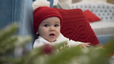 Yastık ile büyük bir sandalyede oturan ve hediye ile eğlenmek beyaz bobble ile kırmızı şapkalı sevimli bebek yakın