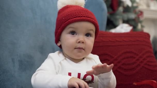 Close up de criança doce vestindo bobble chapéu sentado em cadeira de braço confortável com travesseiro e brincando com presente de Natal — Vídeo de Stock